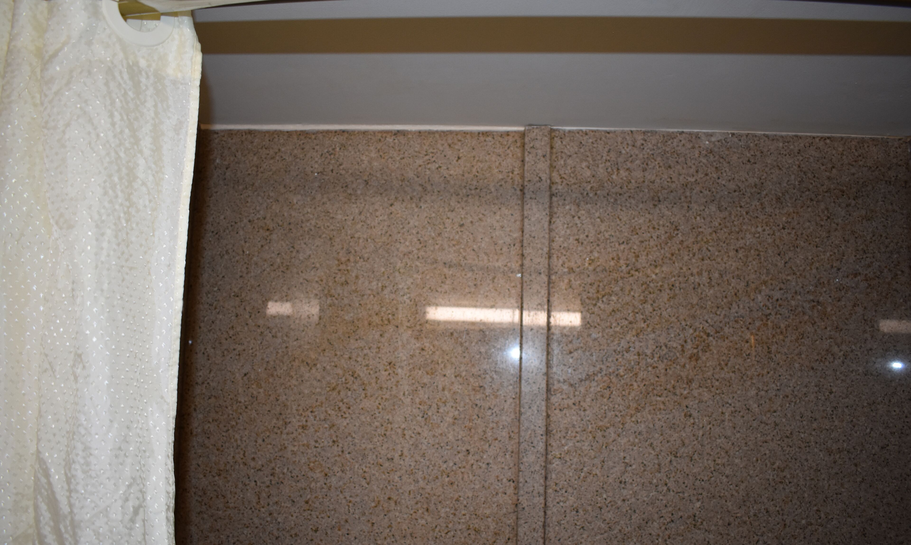 A bathroom with a granite countertop and a white shower curtain.