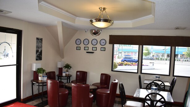 A restaurant interior with red leather chairs, a chandelier, wall clocks, and a view of the street through large windows. - MHO Hotel Bordentown (Bordentown)