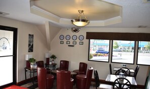 A restaurant interior with red leather chairs, a chandelier, wall clocks, and a view of the street through large windows.