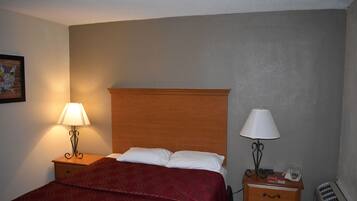 A hotel room with a wooden headboard, a bed with white and red bedding, two bedside tables with lamps, a small drawer, and a wall-mounted telephone.