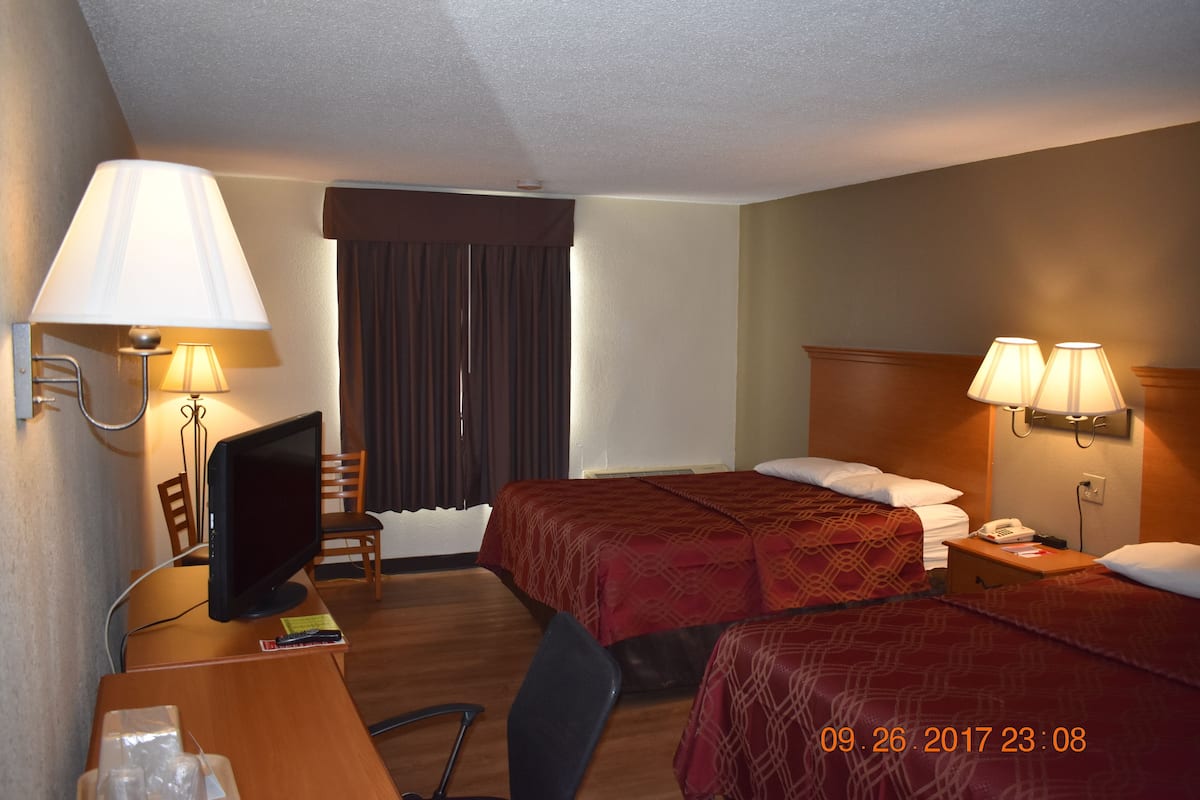 Une chambre d’hôtel avec deux lits, un bureau avec un ordinateur, une chaise et des lampes.