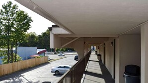 A covered outdoor area with a metal railing, a trash bin, and a view of a parking lot with cars. - MHO Hotel Bordentown (Bordentown)