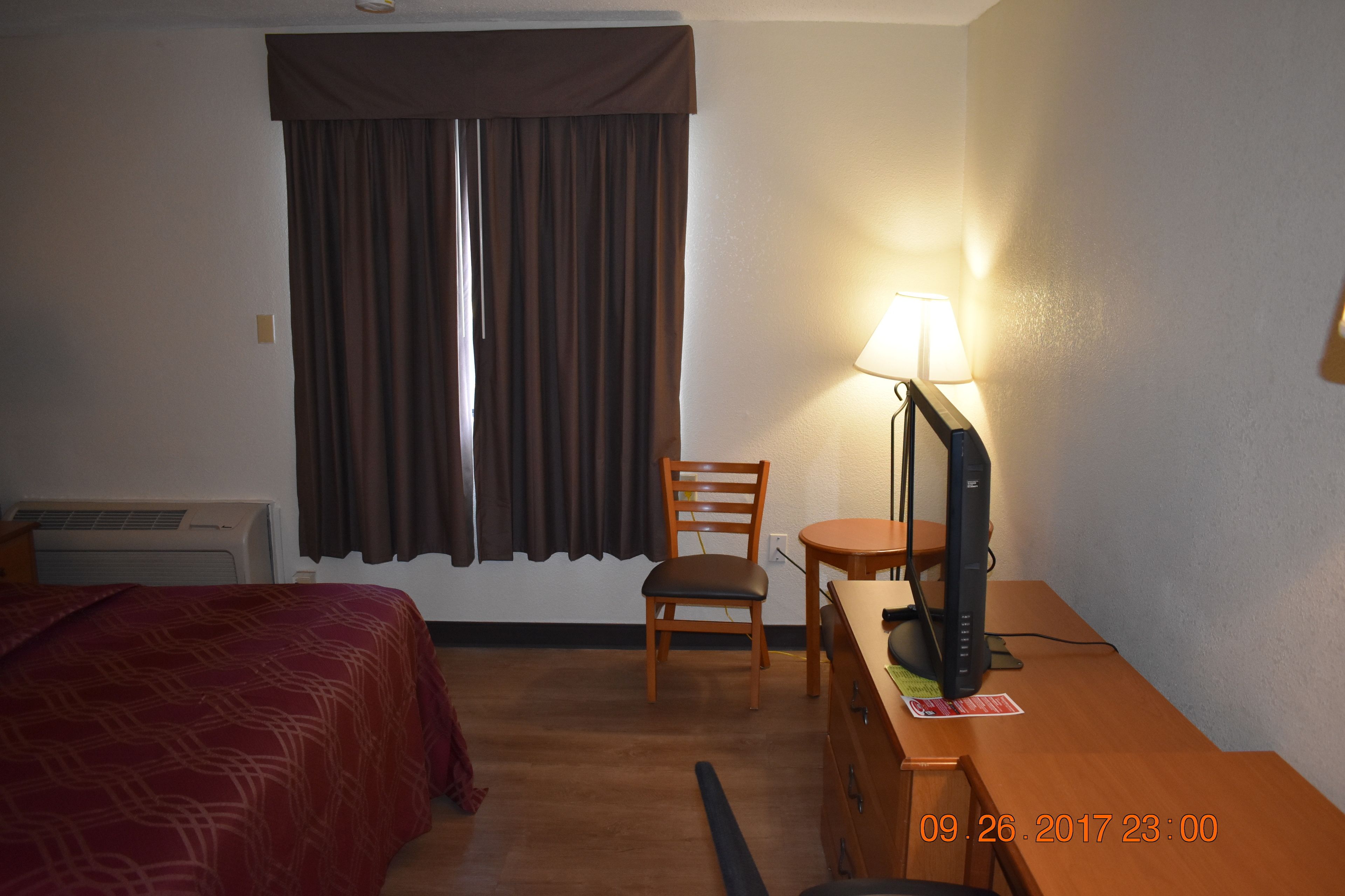 Una habitación de hotel con una cama, un escritorio con computadora, una silla y una ventana con cortinas.