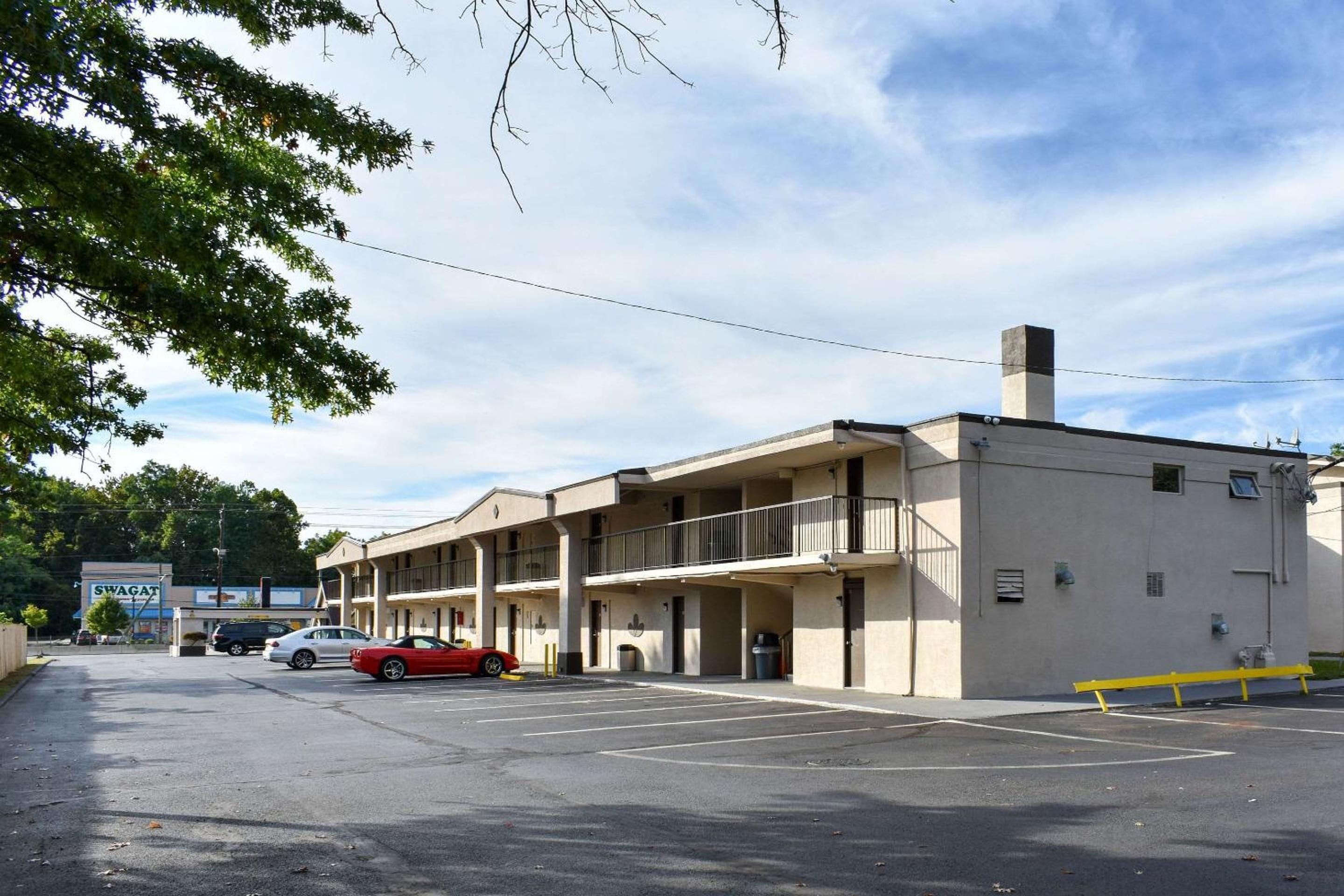 A multi-story motel with a parking lot, a red car parked in the lot, and a sign for 'SWAGAT' in the background.