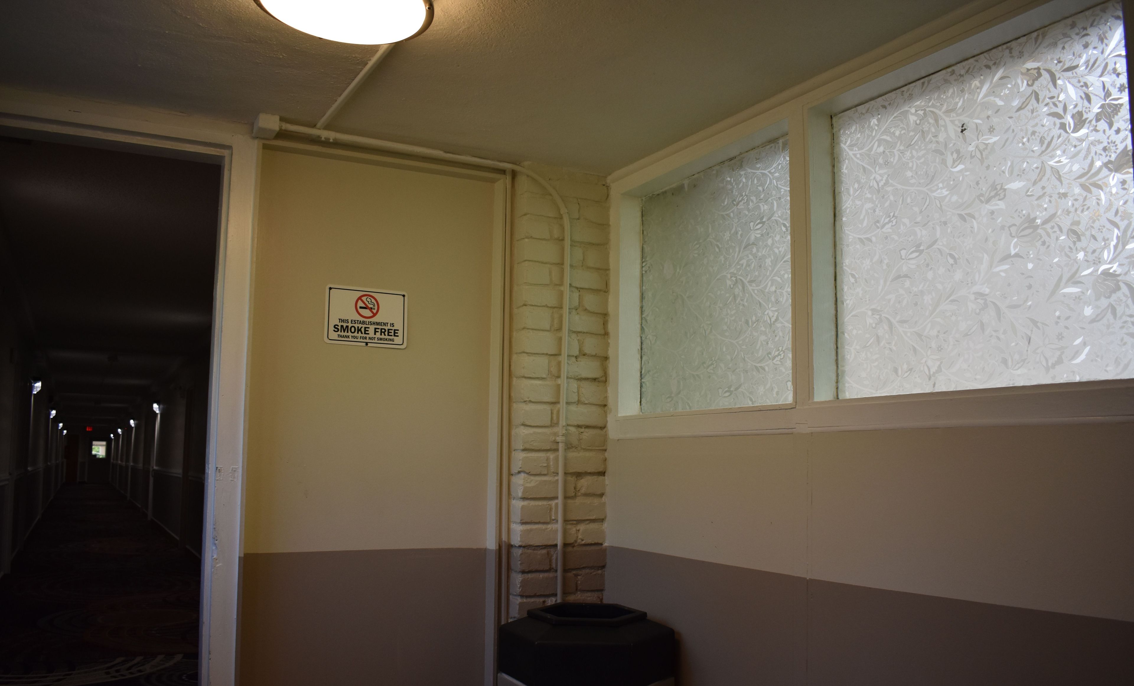 A smoke-free sign in a hallway with a brick wall and a window with frosted glass.