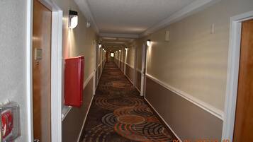 A hotel hallway with a patterned carpet, doors on both sides, and a red object on the left wall.