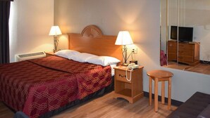 A hotel room with a bed, bedside lamps, a nightstand, a small table, a television, and a dresser. - MHO Hotel Bordentown (Bordentown)