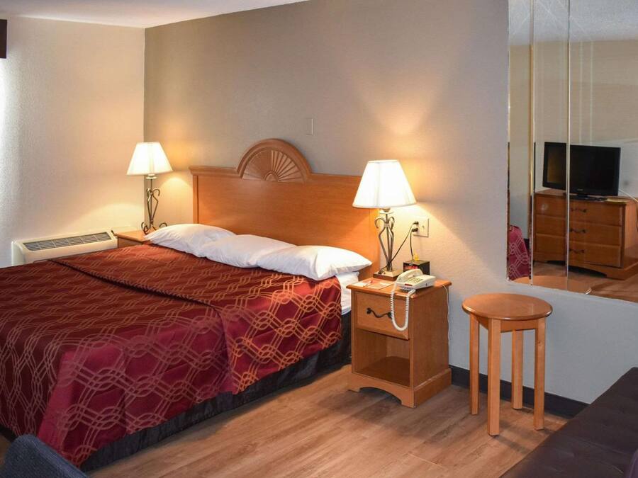 A hotel room with a bed, bedside lamps, a nightstand, a small table, a television, and a dresser.