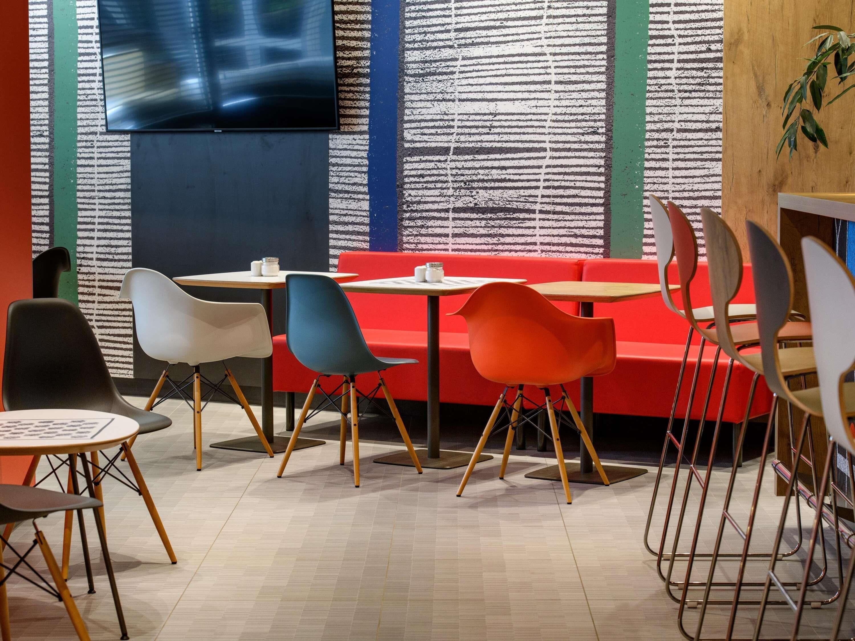 Un café moderne avec des chaises colorées, un canapé rouge et un téléviseur fixé au mur.
