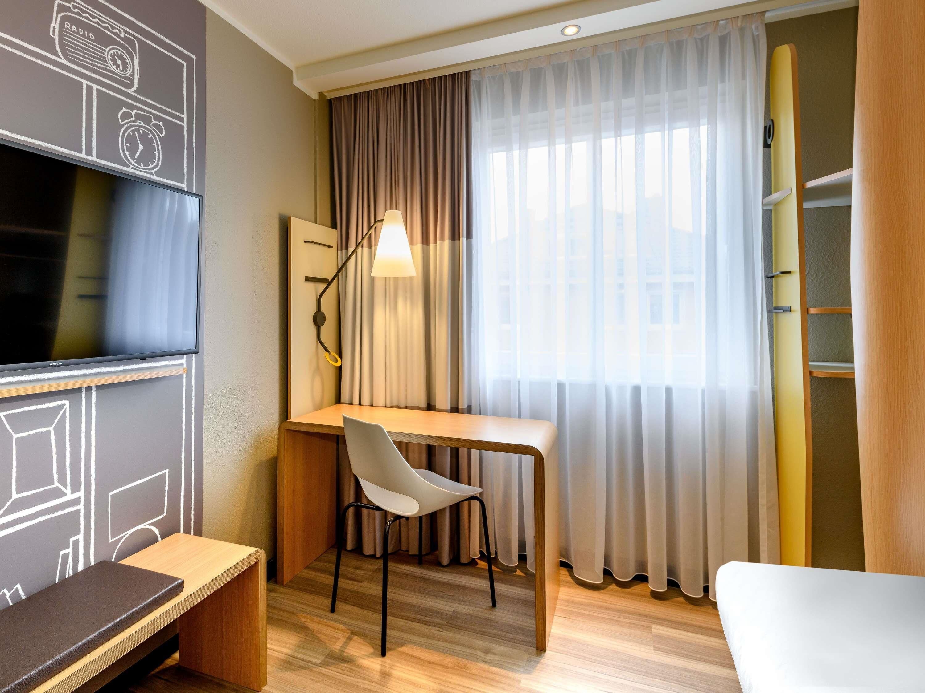 Ein Hotelzimmer mit Schreibtisch, Stuhl, Fernseher und Vorhängen.