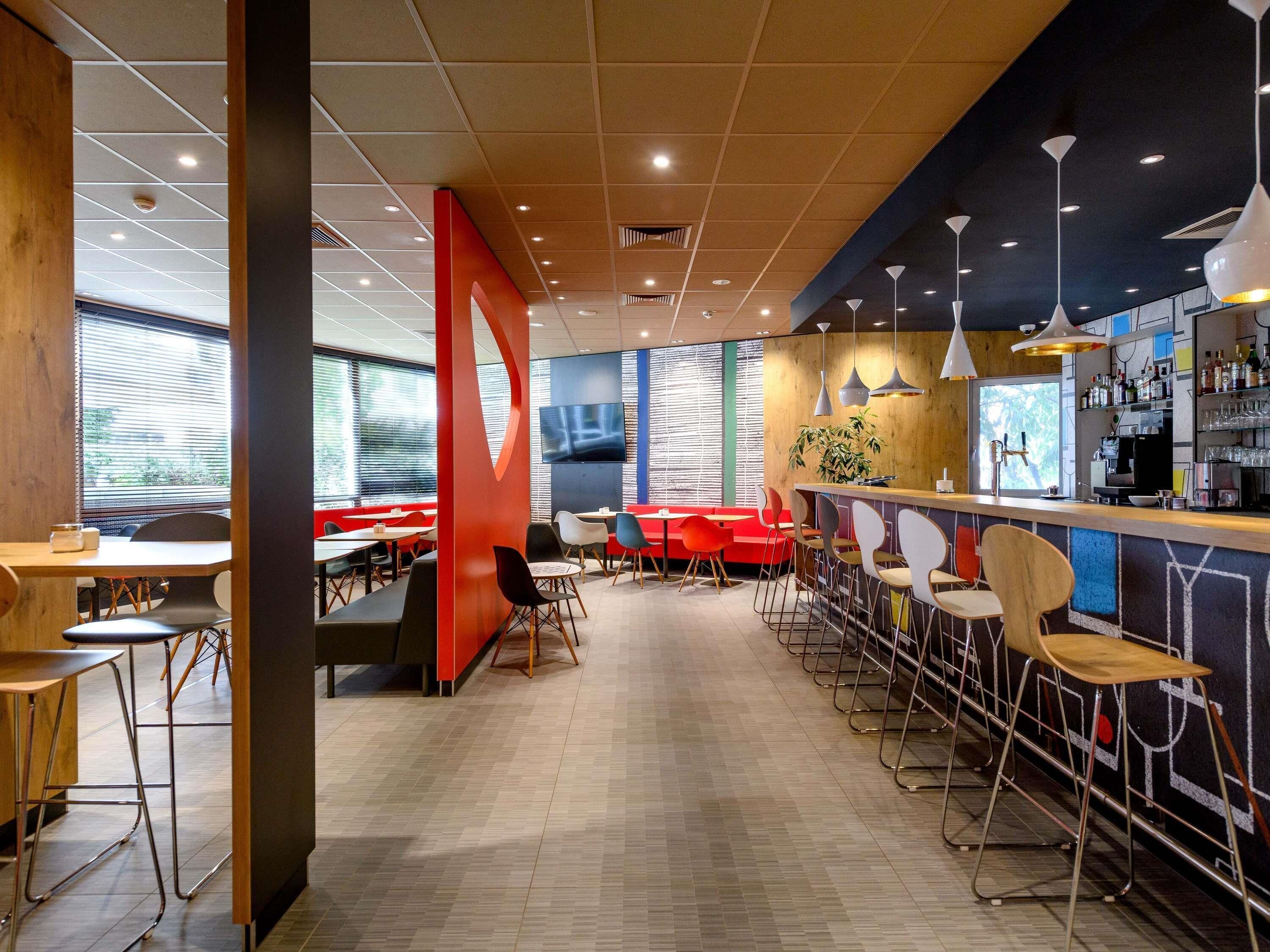 Una cafetería moderna con una barra alargada, varias zonas de estar y una gran pantalla de televisión en la pared.
