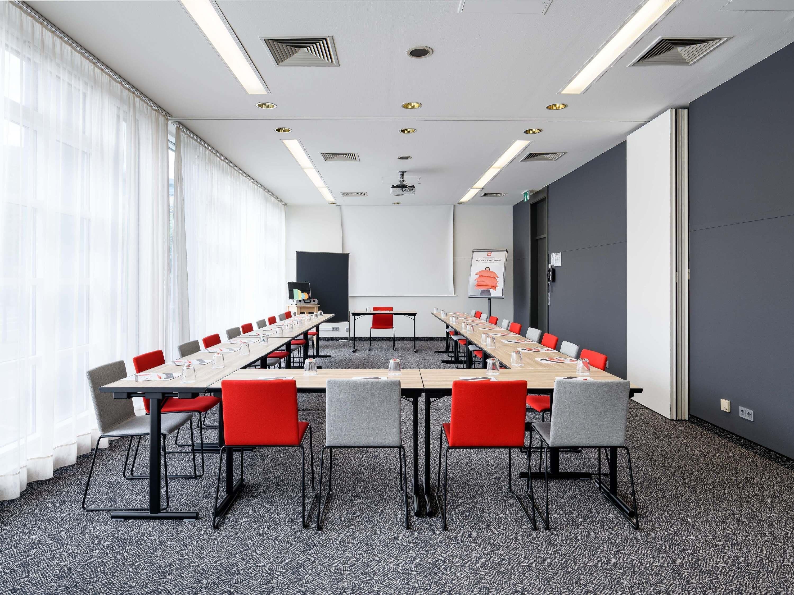 A conference room with a long table, red and grey chairs, a projector, and a whiteboard.