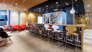 Un área de bar moderna con una barra alargada, diversas opciones de asiento como taburetes y sillas, y una variedad de lámparas colgantes.