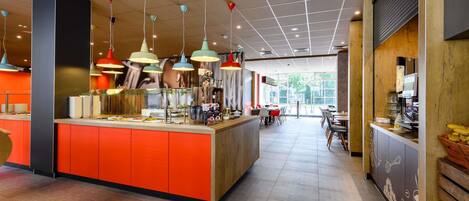 A modern cafe interior with a central island counter, multiple hanging pendant lights, and a view of the outdoors through large windows.