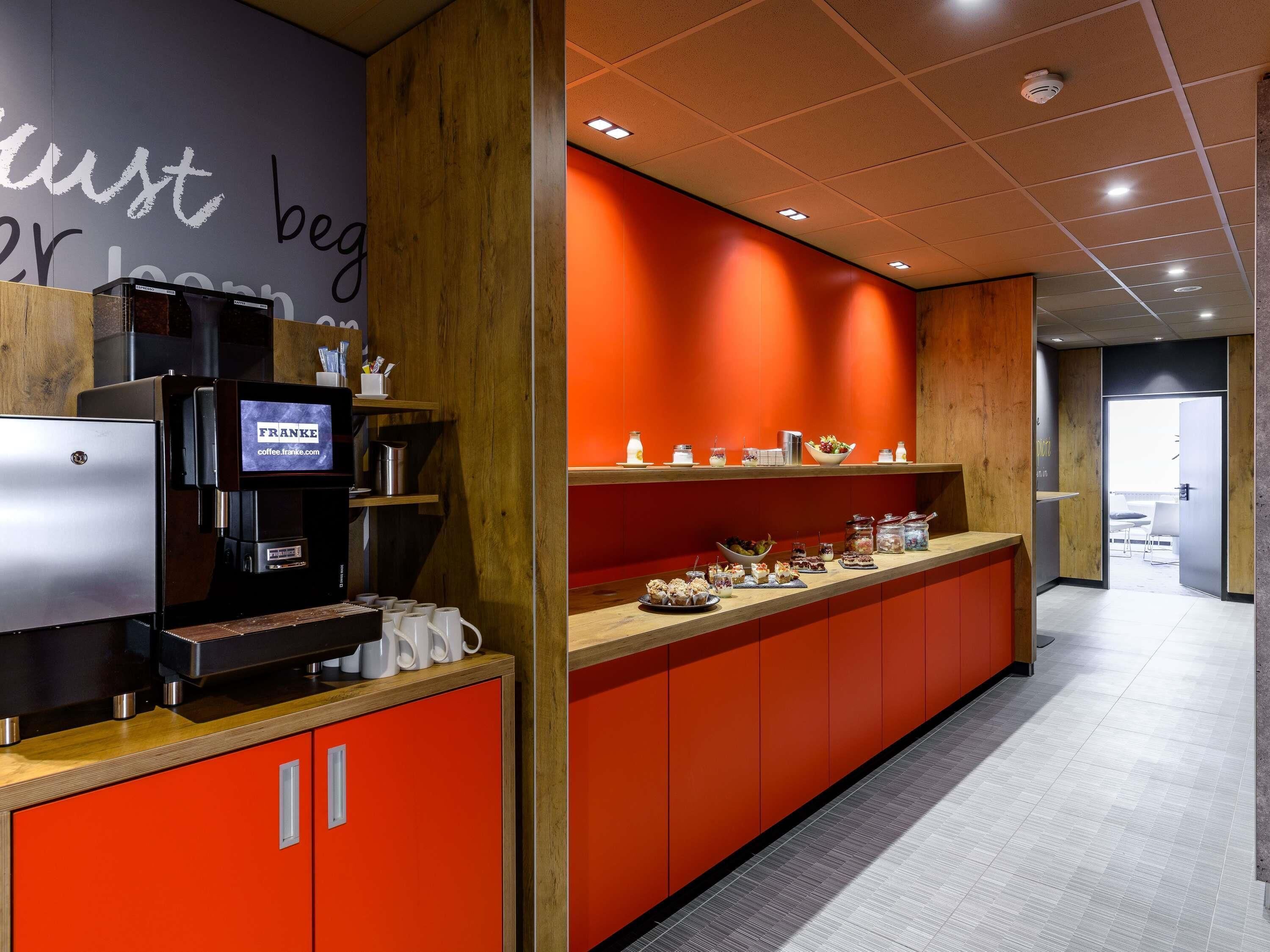 A modern coffee station with a coffee machine, a digital display, and a variety of food items on a counter.