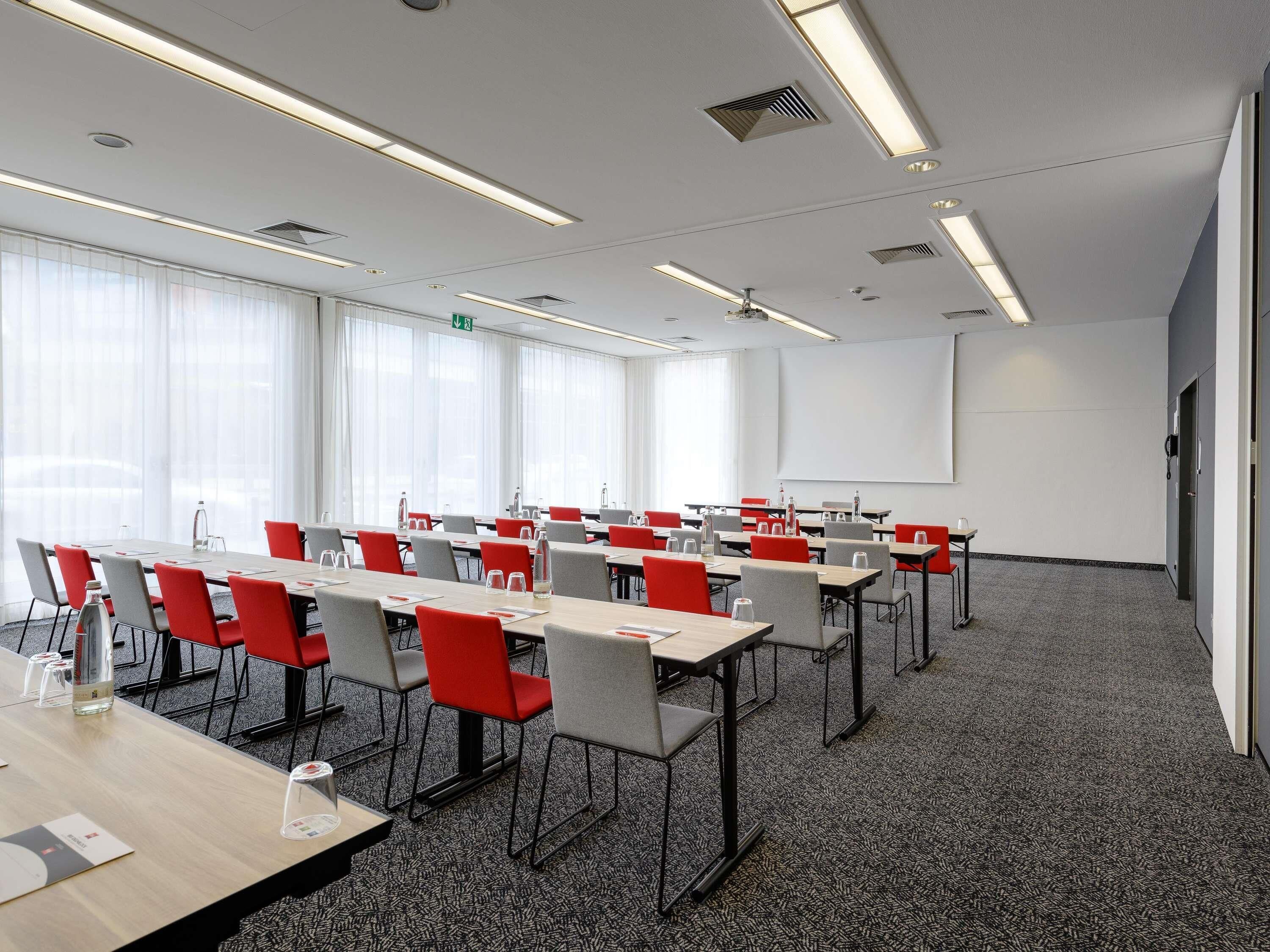 Een vergaderzaal met tafels, stoelen, een projectiescherm en een vloerbedekking.