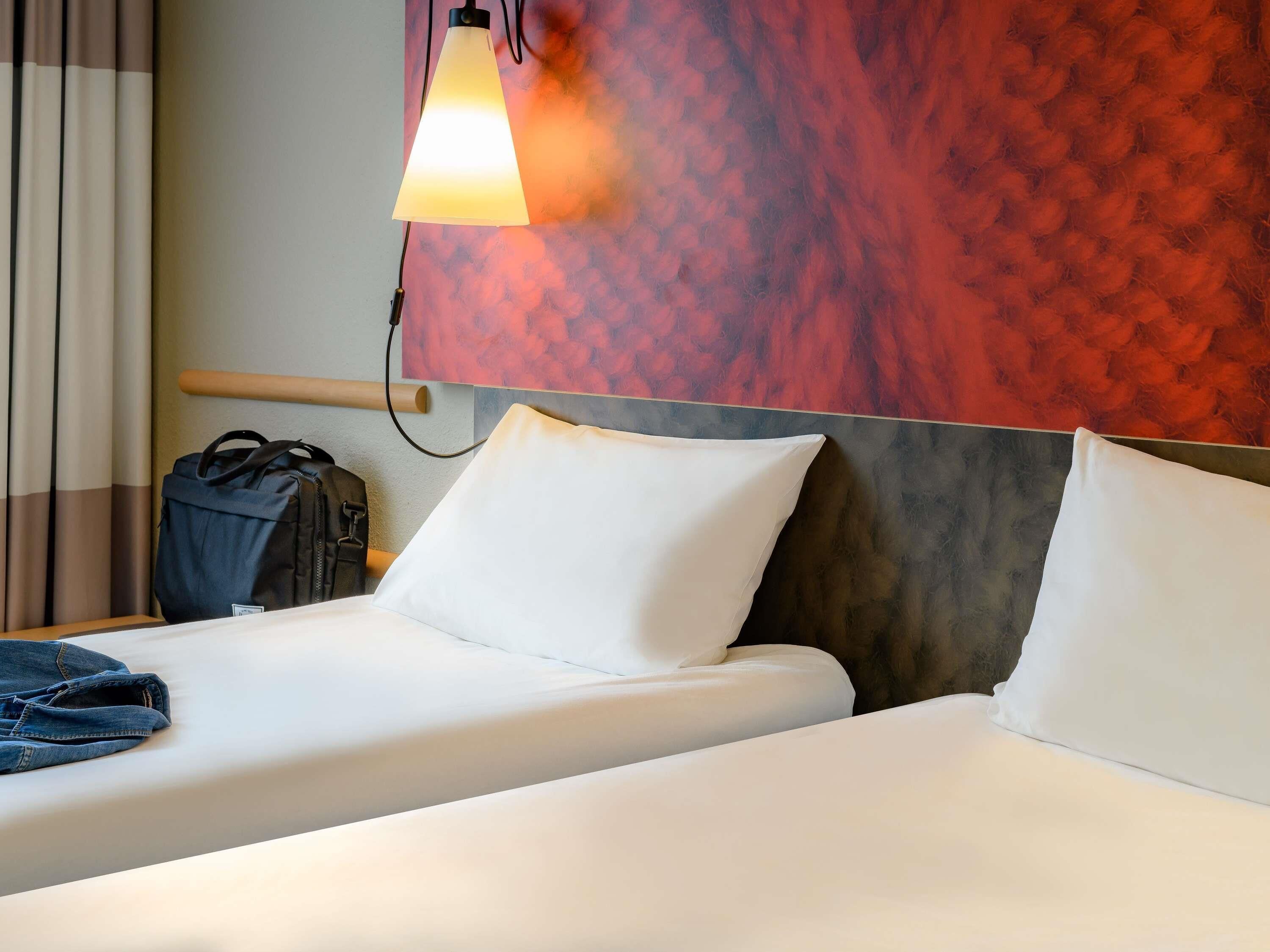 A hotel room with two beds, a nightstand, a lamp, and a wall with a textured pattern.