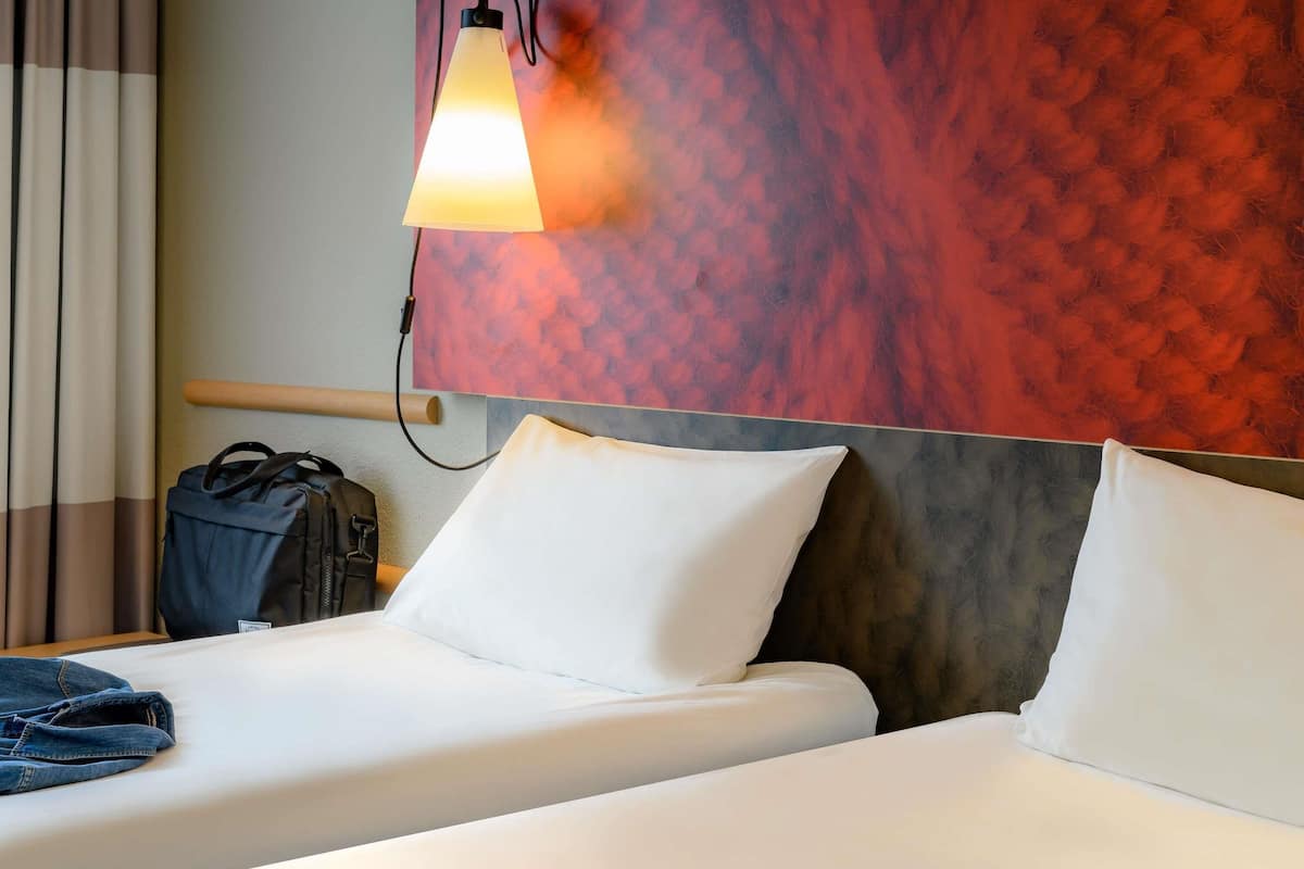 A hotel room with two beds, a nightstand, a lamp, and a wall with a textured pattern.