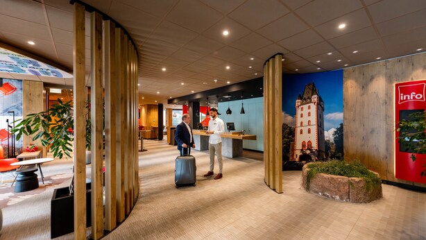 Un moderno vestíbulo de hotel con separadores de madera, un mostrador de recepción y un mural de un castillo.