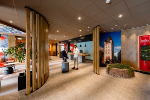 A modern hotel lobby with wooden partitions, a reception desk, and a mural of a castle. - ibis Mainz City (Mainz)