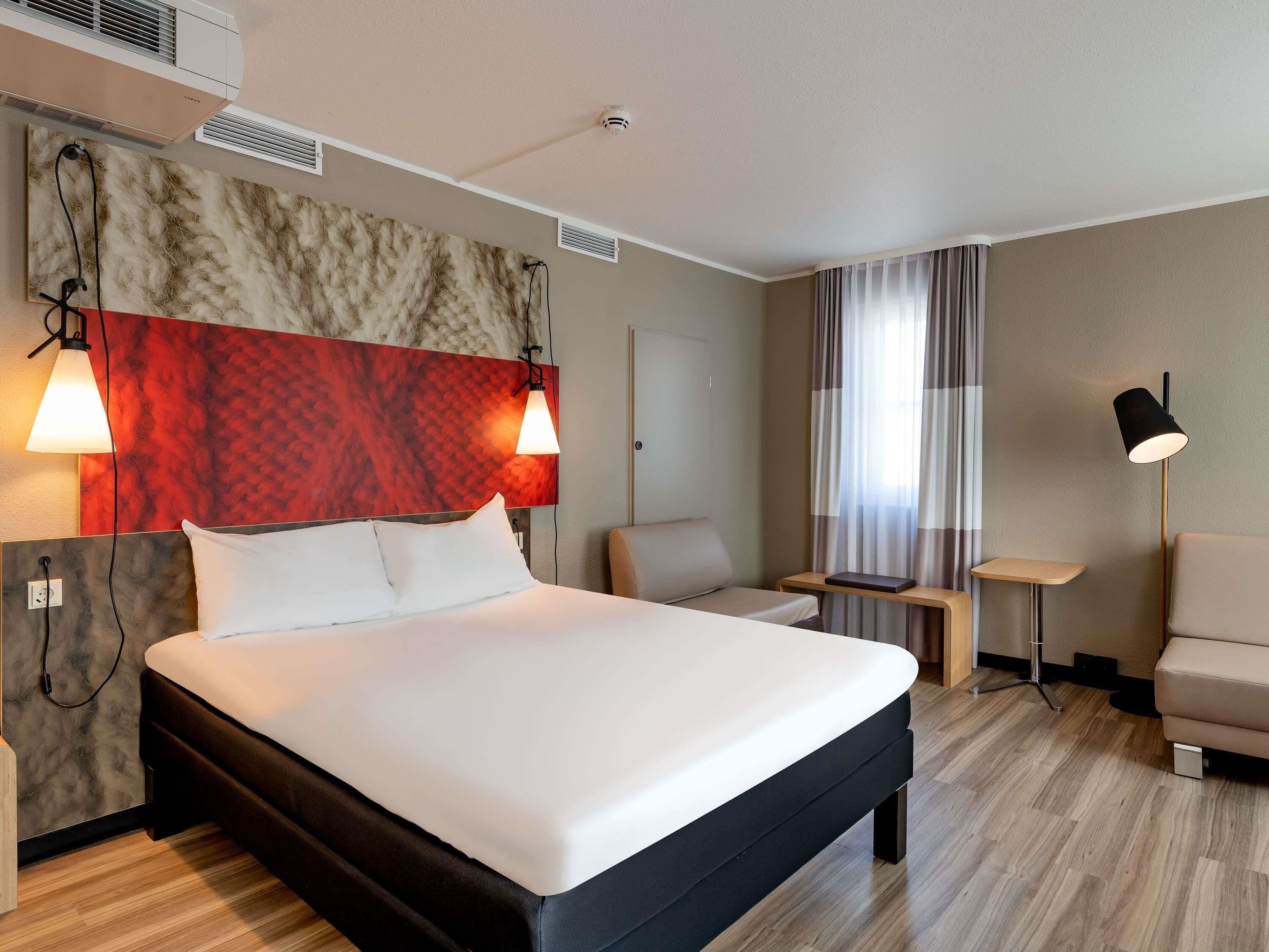 A modern hotel room with a large bed, two bedside lamps, a desk, a chair, and a floor lamp.