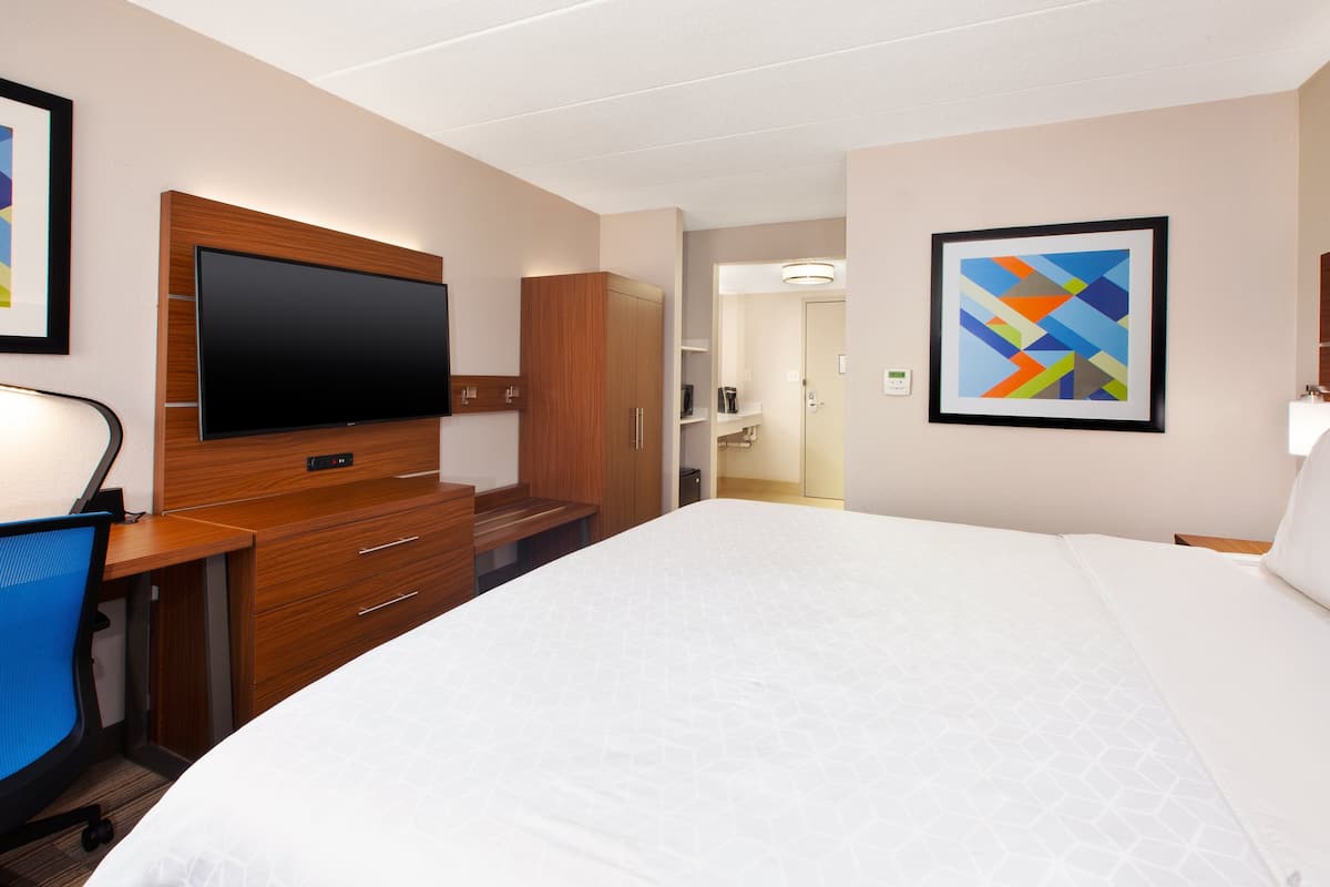 A hotel room with a large bed, a desk with a chair, a flat-screen TV, wooden cabinets, and a framed picture on the wall.