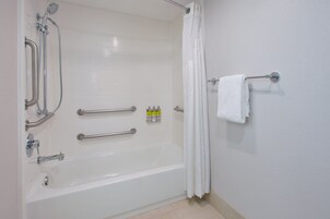 Un baño con bañera, barras de apoyo, cabezal de ducha y perchero.