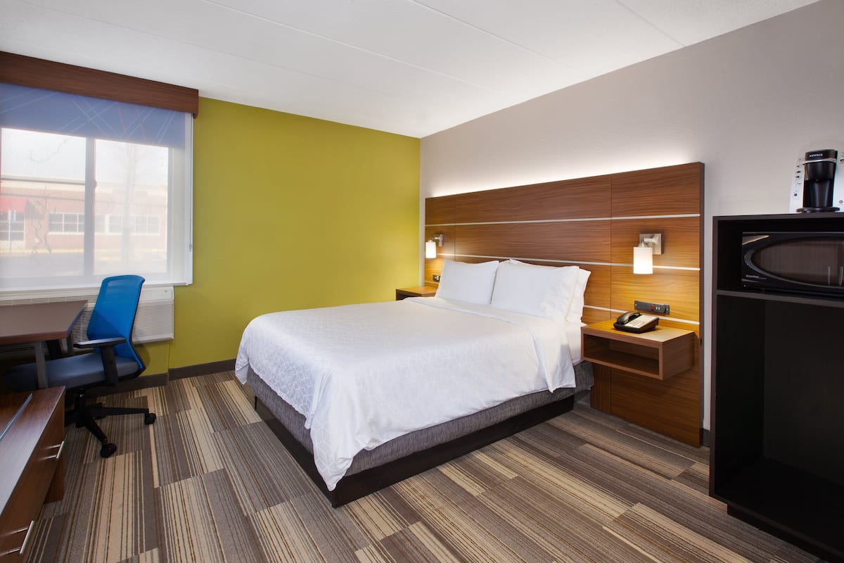 A hotel room with a bed, a desk, a chair, a nightstand, and a microwave.