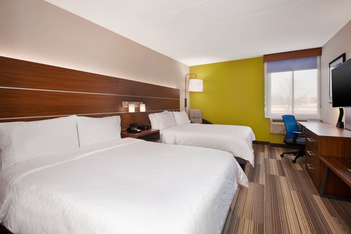 A hotel room with two beds, a desk, a chair, a TV, and a window with blinds.