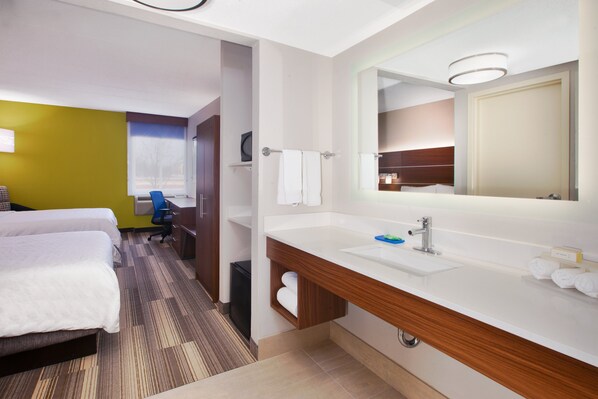 A hotel room with a large bed, a desk, a chair, a bathroom with a sink and mirror, and a window with blinds. - Holiday Inn Express Fairfax - Arlington Boulevard by IHG (Fairfax)