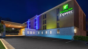 Un edificio de Holiday Inn Express con un diseño moderno, que cuenta con un letrero grande, un acceso cubierto y un estacionamiento.