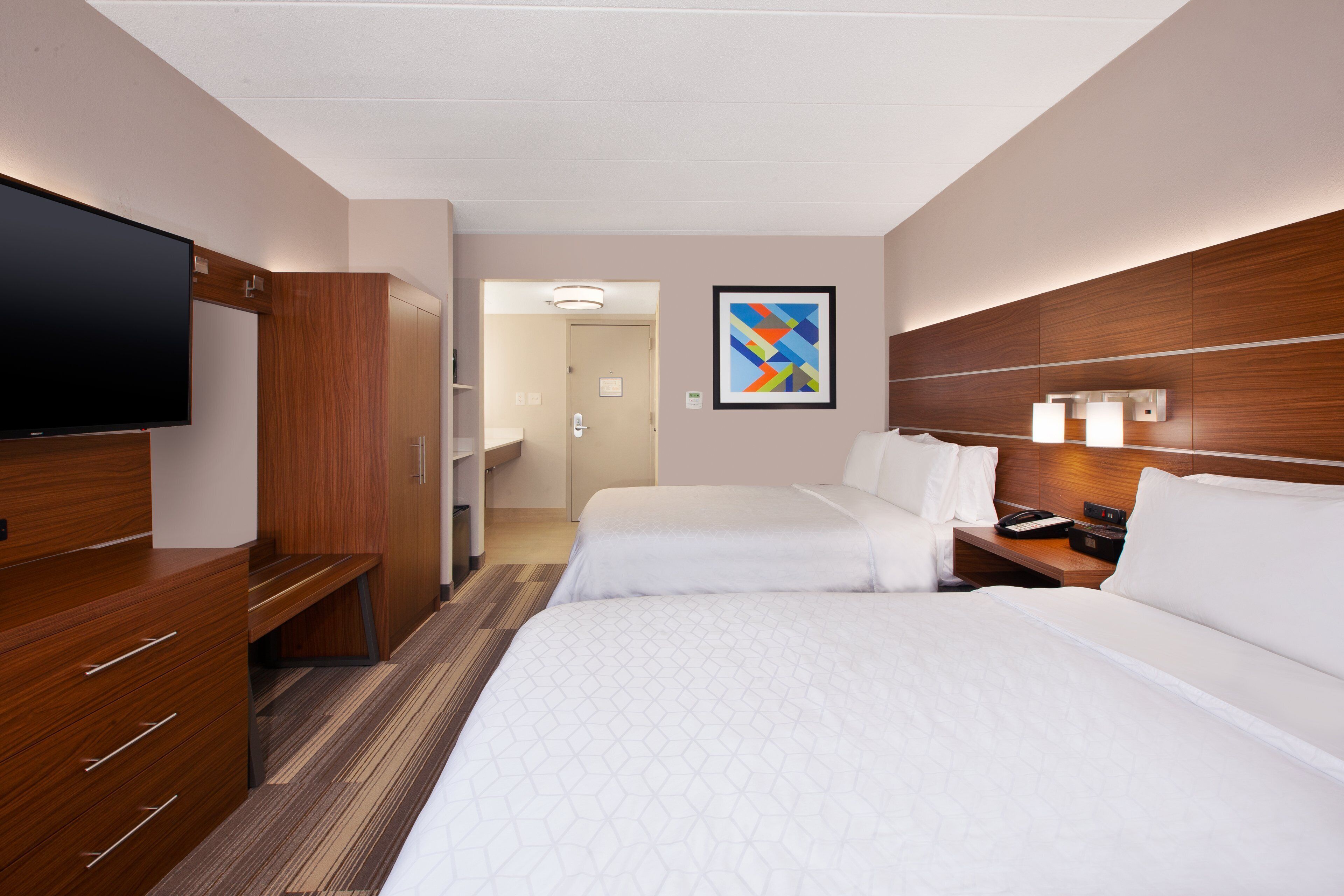 A hotel room with two beds, a TV, a desk with a phone, and a painting on the wall.