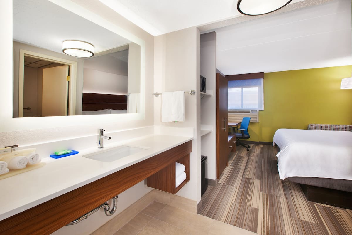 A hotel room with a large bathroom vanity, a bed, and a view of the outside.