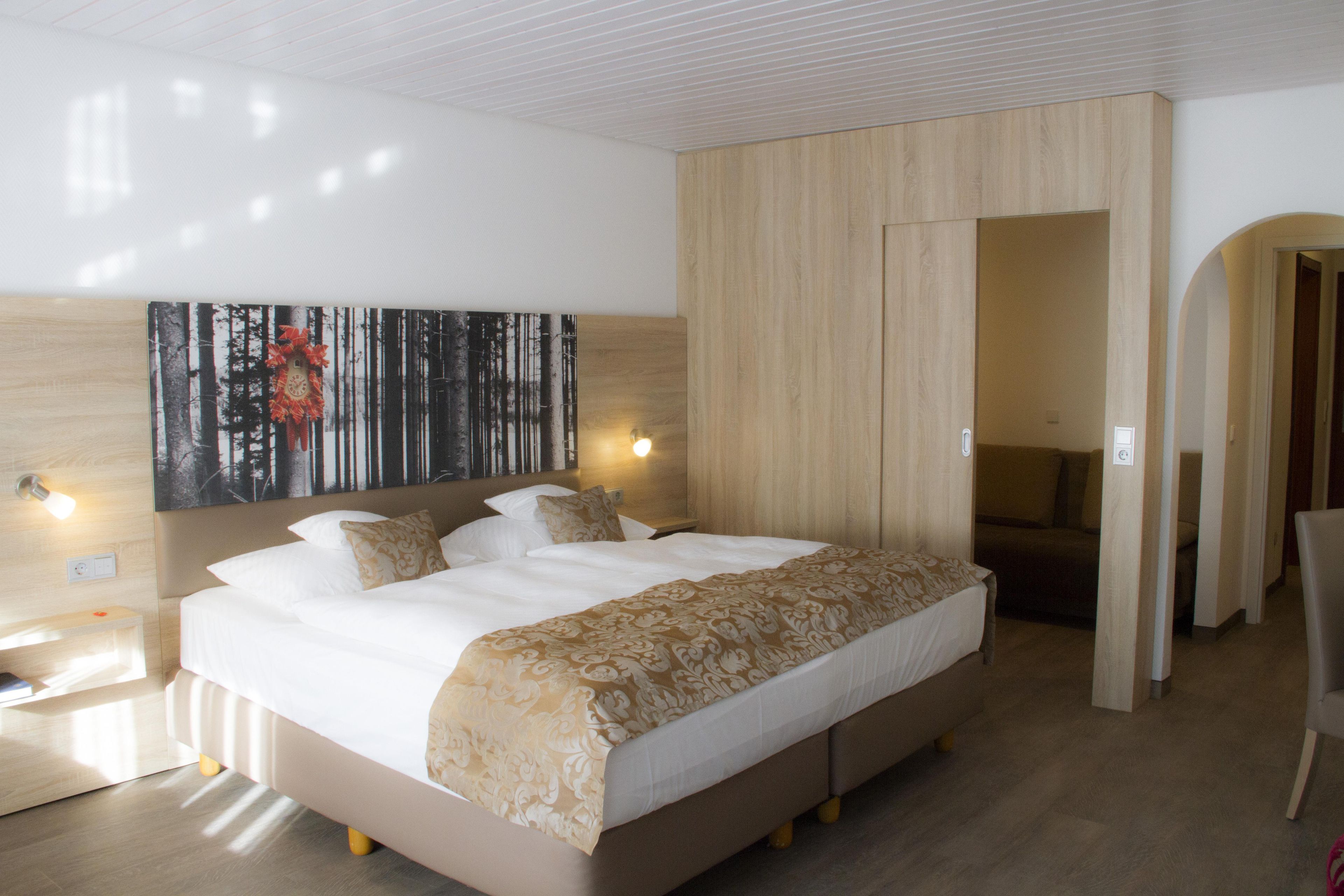A modern hotel room with a large bed, a headboard with a clock, a painting above the bed, and a wooden wardrobe.