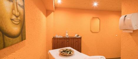 A room with a wooden ceiling, a wall-mounted towel dispenser, a wooden cabinet with a 'Relax' sign, and a white towel on a table.