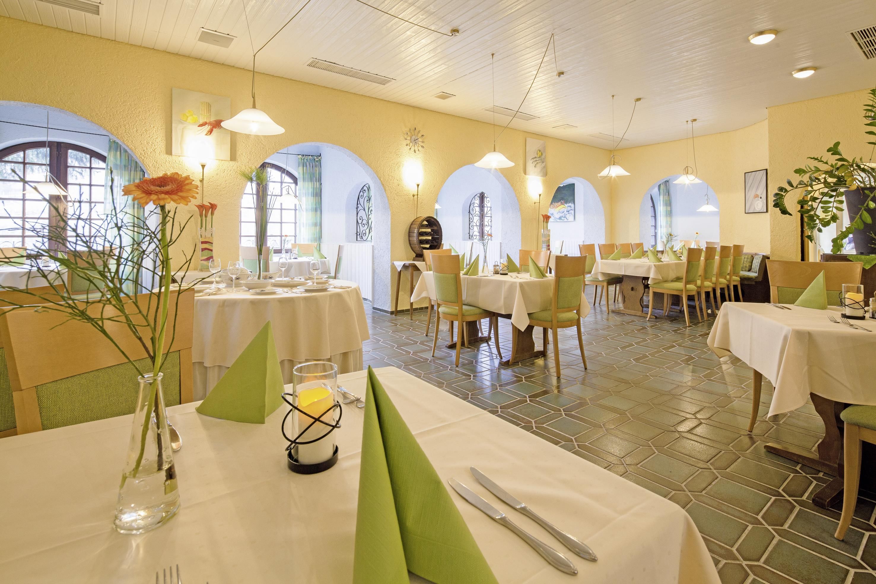 A dining area with tables set for two, featuring a tiled floor and arched windows.