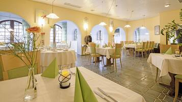 A dining area with tables set for two, featuring a tiled floor and arched windows.