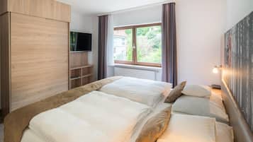 A hotel room with two beds, a TV, a window with curtains, and a radiator.