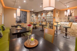 Un restaurante con zona de comedor central, barra y estantería llena de revistas.