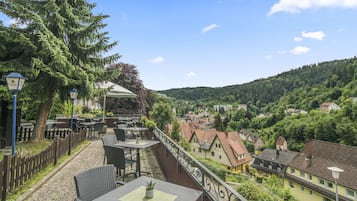 A terrace with outdoor seating, overlooking a town and forested hills.