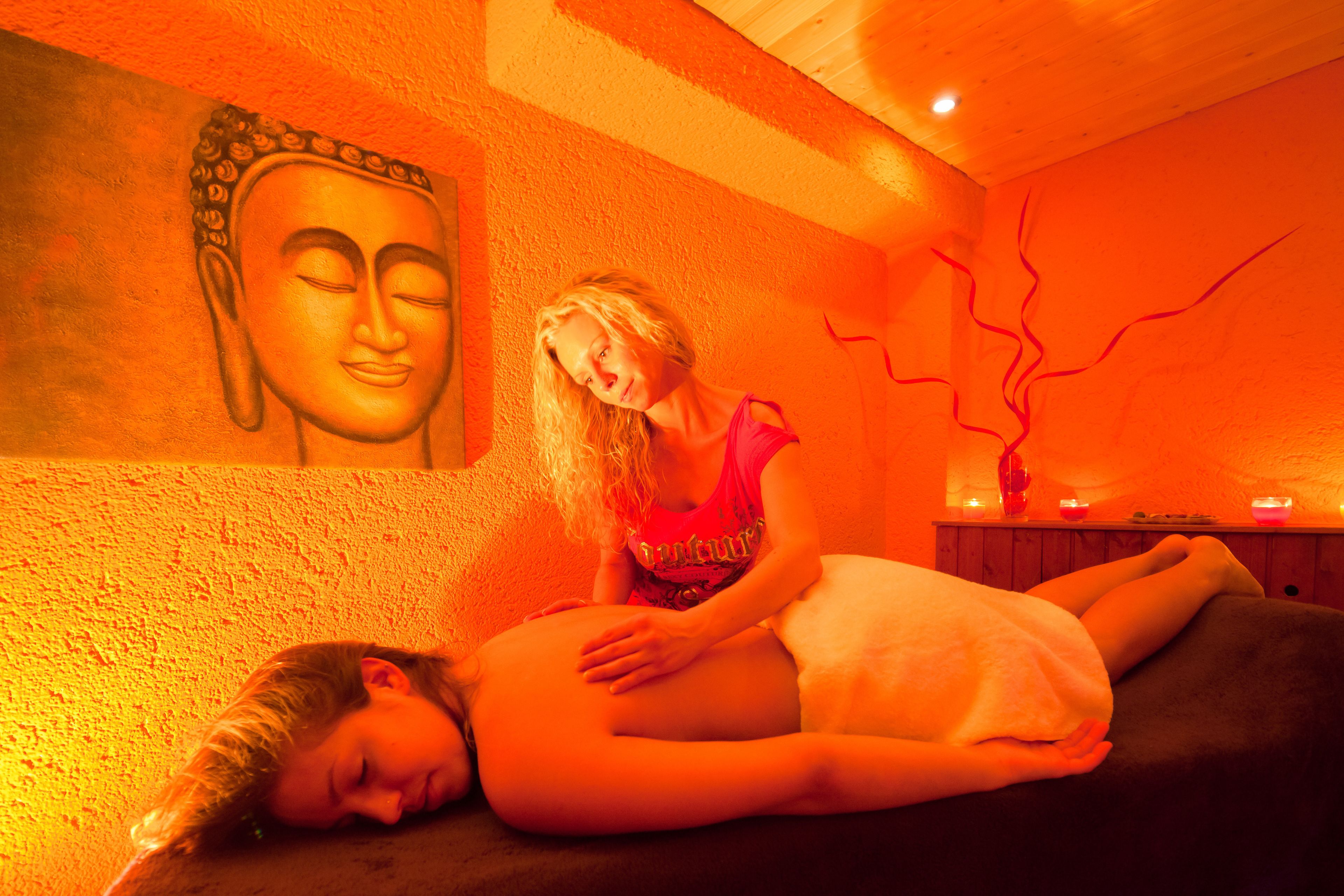 A massage therapy room with a large Buddha statue on the wall, a wooden ceiling, and candles on a table.