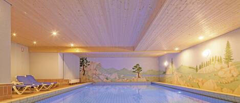 A swimming pool with a tiled floor and wooden ceiling, surrounded by lounge chairs and a mural depicting a mountainous landscape.