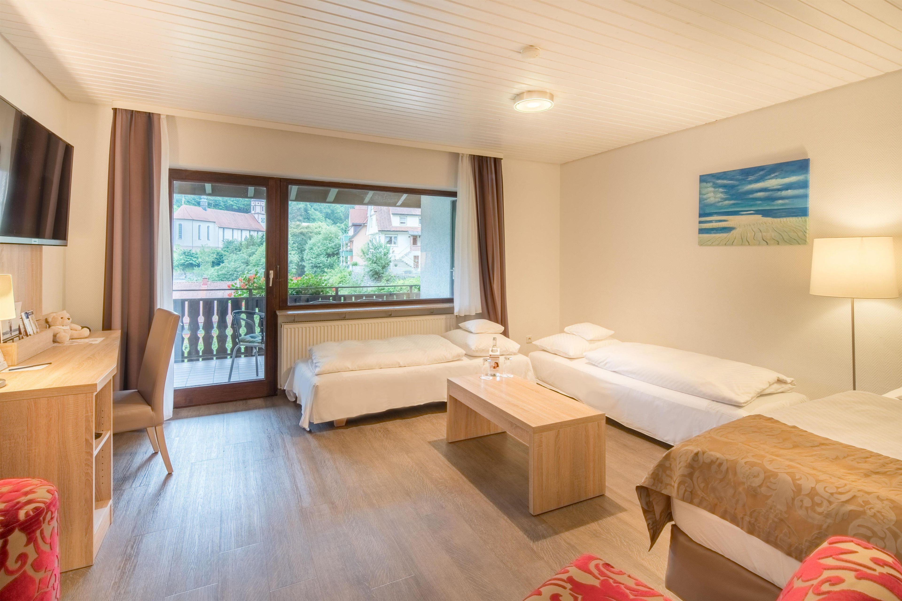 A hotel room with two beds, a desk, a chair, a TV, and a window with a view of buildings and trees.