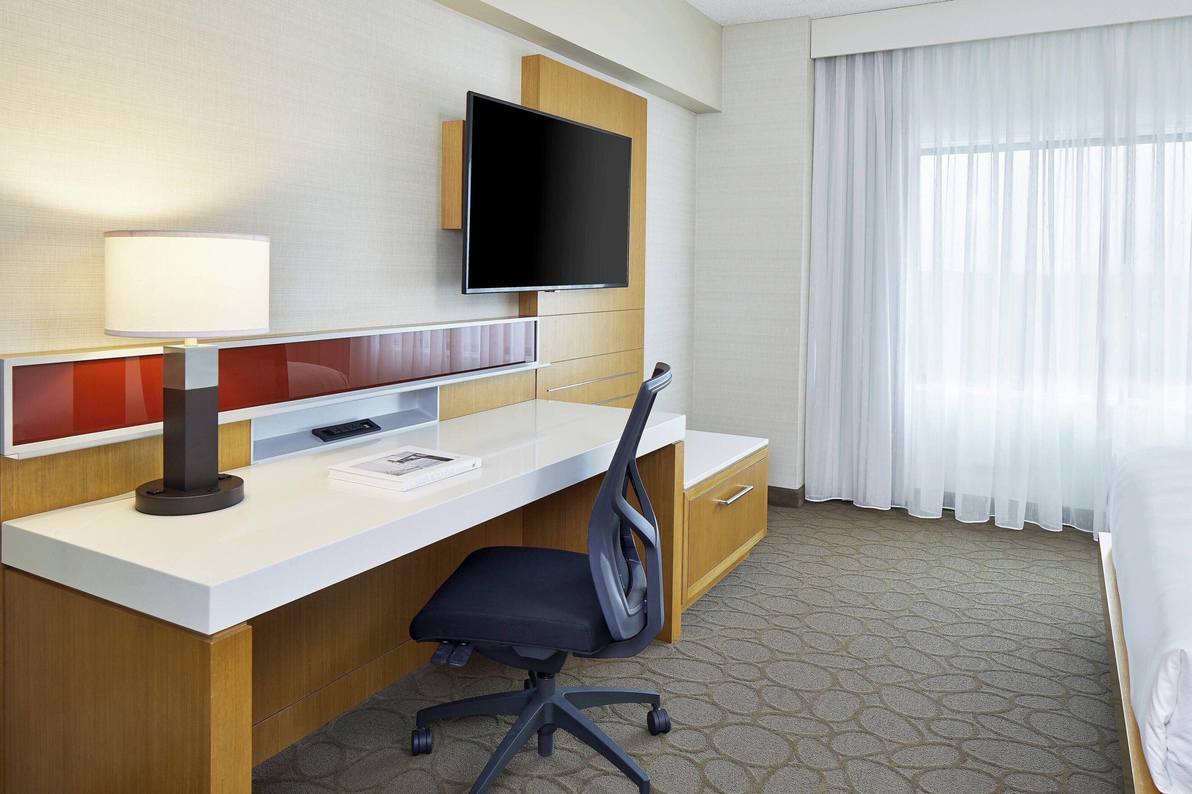 Ein Hotelzimmer mit Schreibtisch, Stuhl, Fernseher und Bett.