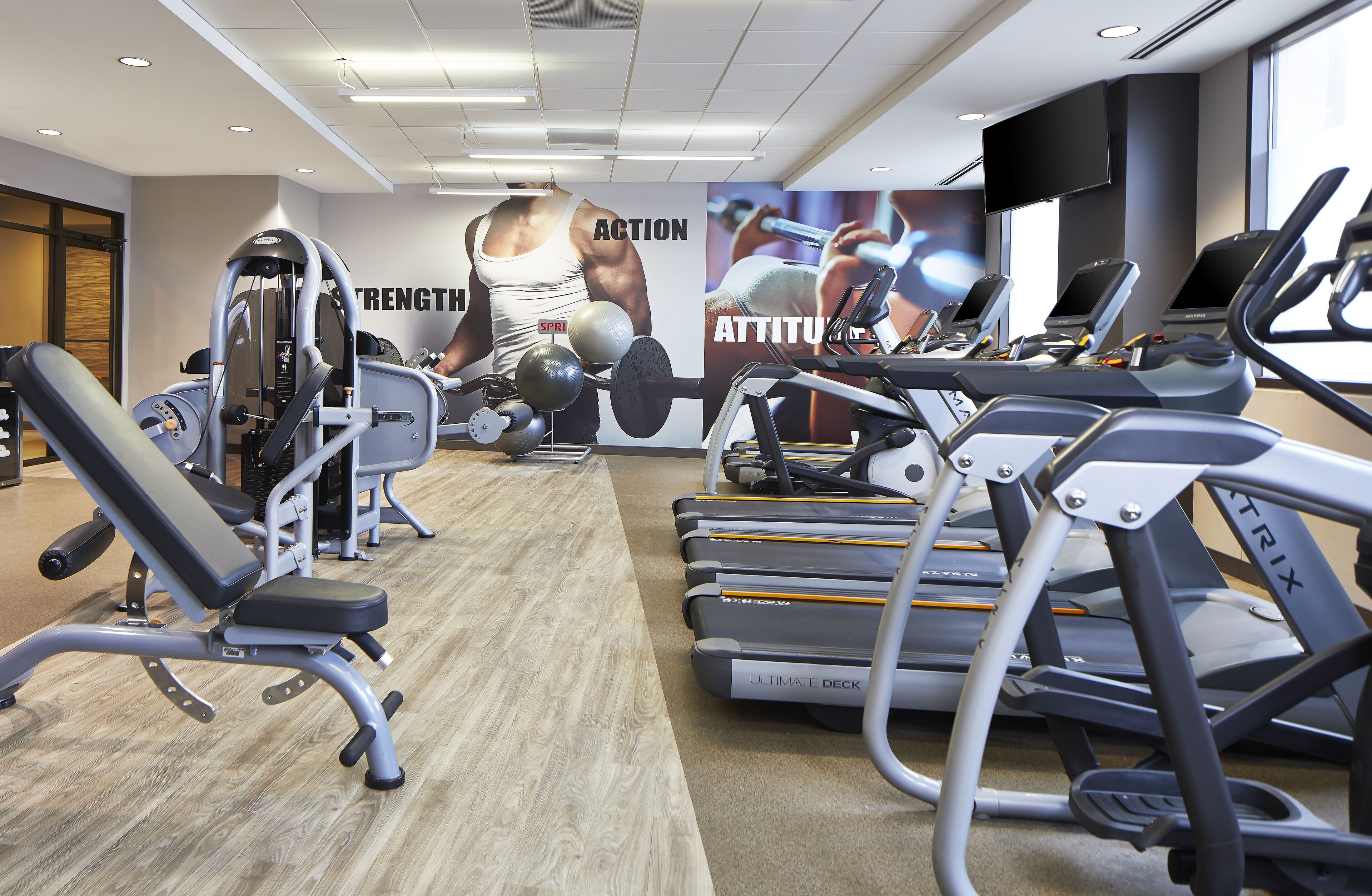 A gym with treadmills, weight machines, and a large motivational poster on the wall.