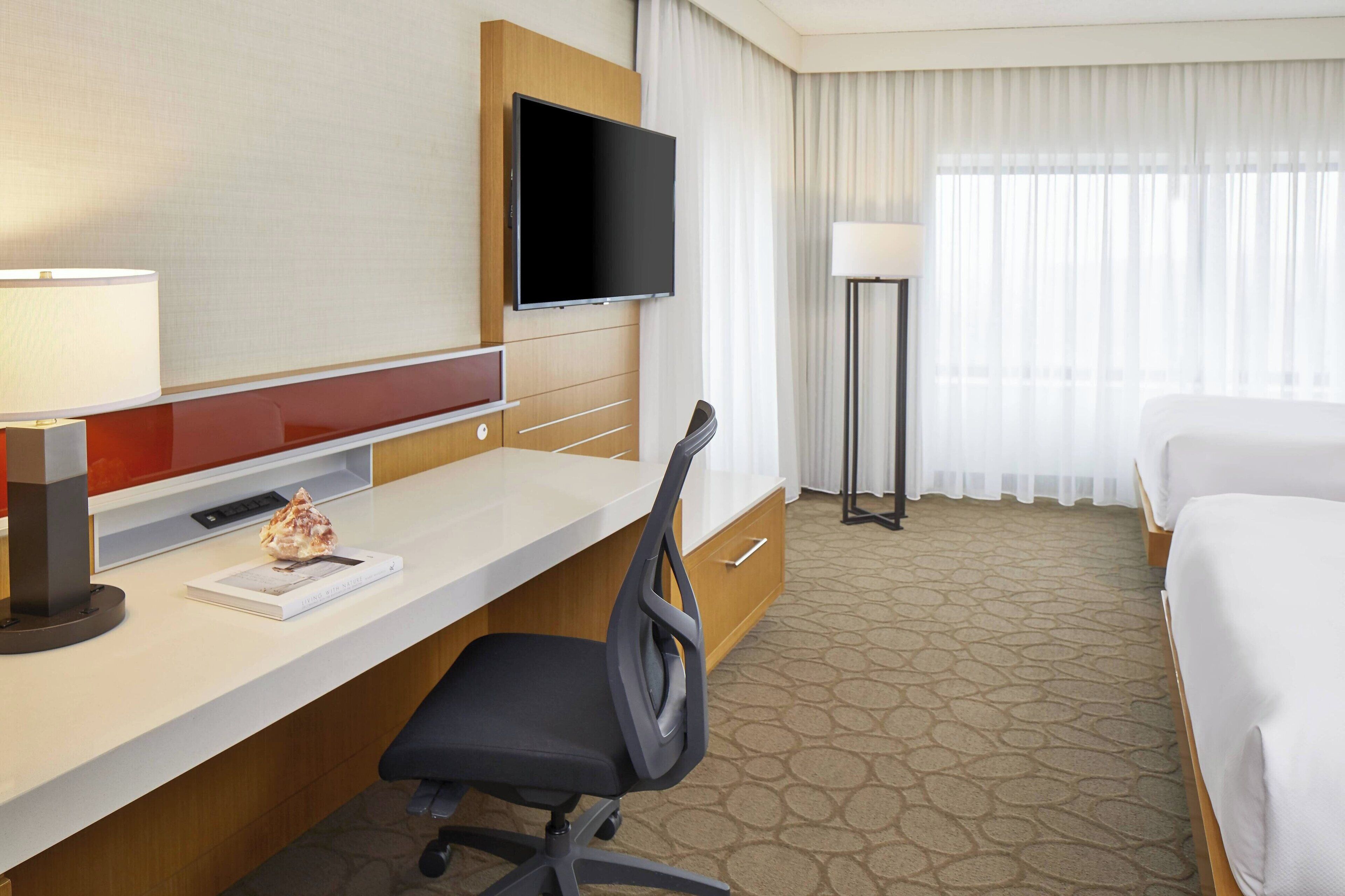 Una habitación de hotel con cama, escritorio, silla, televisión y lámpara.