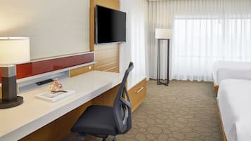 Una habitación de hotel con cama, escritorio, silla, televisión y lámpara.