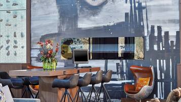 A modern bar area with a wooden counter, multiple bar stools, and a large abstract painting on the wall.