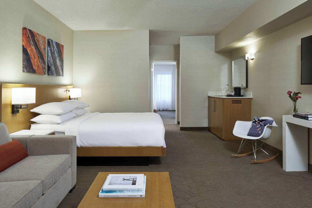 Hotellihuone, jossa on sänky, sohva, työpöytä, tuoli, sohvapöytä ja taulu seinällä.