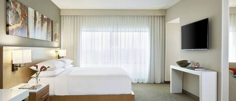 A hotel room with a bed, bedside table, lamp, artwork, and a TV.